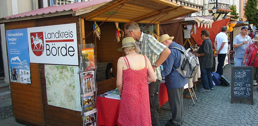 Das Foto zeigt eine Markthütte des Landkreises Börde im Rahmen der Präsentation zum "Sachsen-Anhalt-Tag" 2014 in Wernigerode. Davon und im Umfeld stehen "Besucher / Festteilnehmer", die sich über den Landkreis Börde informieren.