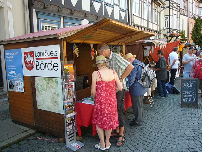 Das Foto zeigt eine Markthütte des Landkreises Börde im Rahmen der Präsentation zum "Sachsen-Anhalt-Tag" 2014 in Wernigerode. Davon und im Umfeld stehen "Besucher / Festteilnehmer", die sich über den Landkreis Börde informieren.