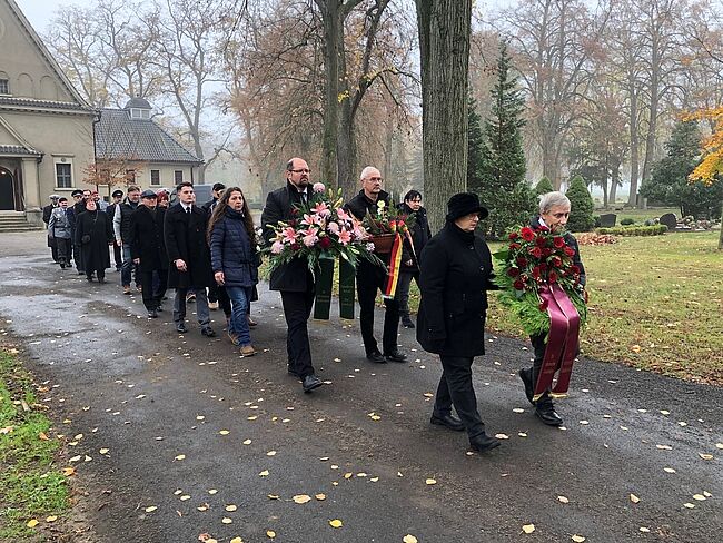 Landkreis Börde / die Stadt Oschersleben hat am Volkstrauertag eine Gedenkveranstaltung durchgeführt. Auch Landrat Martin Stichnoth ist der Einladung des Bürgermeisters gefolgt. Hier der Marsch zum Gedenkstein. Der Landrat mit einem Trauergebinde in den Händen. 