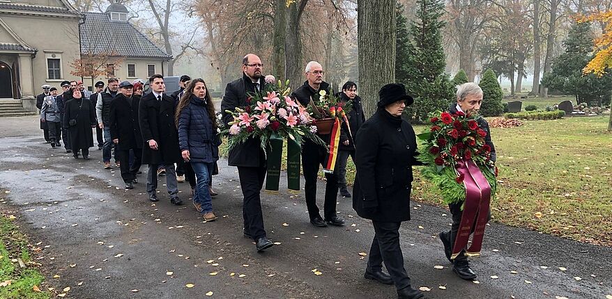 Landkreis Börde / die Stadt Oschersleben hat am Volkstrauertag eine Gedenkveranstaltung durchgeführt. Auch Landrat Martin Stichnoth ist der Einladung des Bürgermeisters gefolgt. Hier der Marsch zum Gedenkstein. Der Landrat mit einem Trauergebinde in den Händen. 