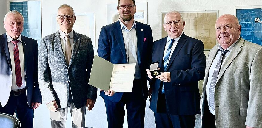 Das Foto zeigt Landrat Martin Stichnoth und Joachim Kunkel mit Urkunde und Erinnerungsmedaille. Daneben 3 Herren des Unternehmens und des Oscherslebener Sportclubs. Das Foto ist aufgenommen in einer Räumlichkeit der "oddesse". 