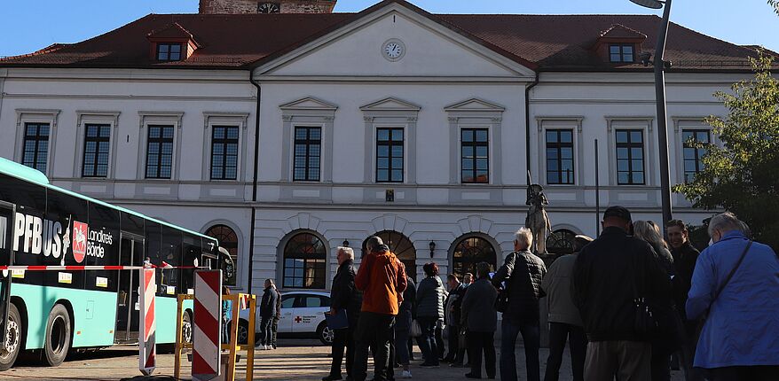 Das Foto zeigt einen Impfbus auf dem Rathausmarkt in Haldensleben. Etwa 30 Personen warten vor dem Bus auf Ihre Impfung. Im Hintergrund sieht man das Rathaus. 